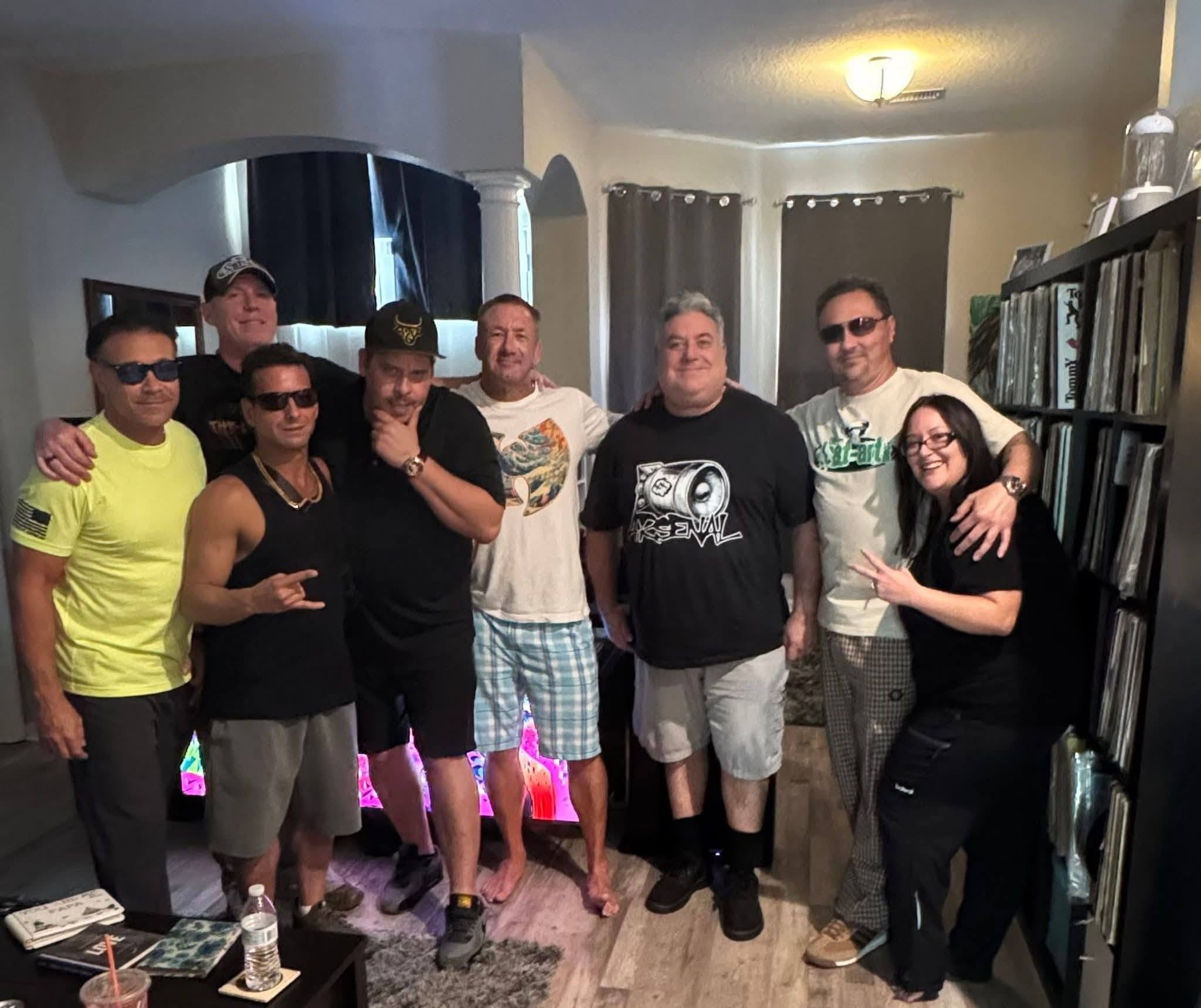 Eight people including DJ Natural Nate® gathered in a living room with vinyl shelves at the Florida show May 2026