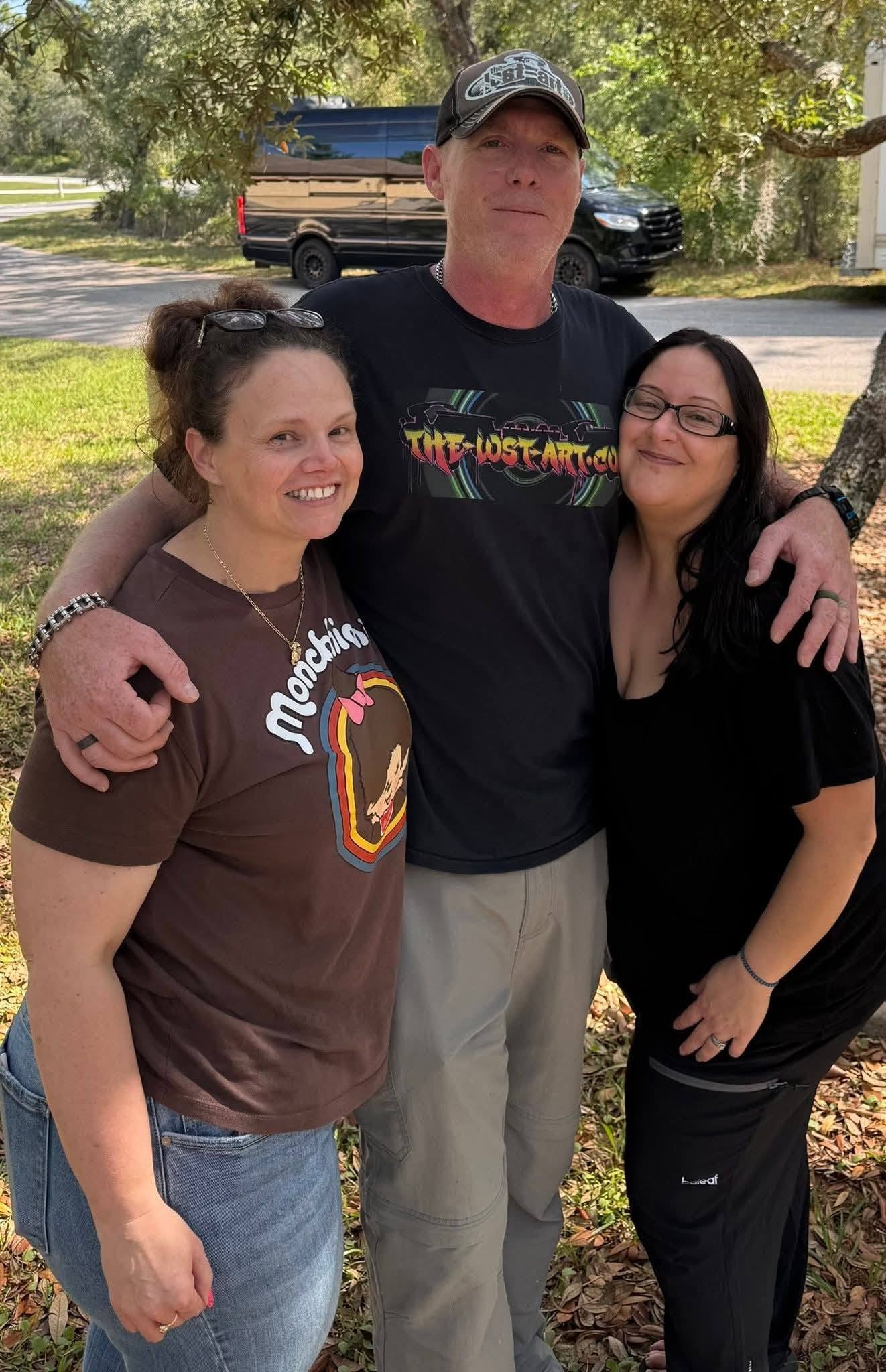Disco Dave in The-Lost-Art.com cap and shirt standing outdoors with two women under oak trees in Homosassa Florida May 2026