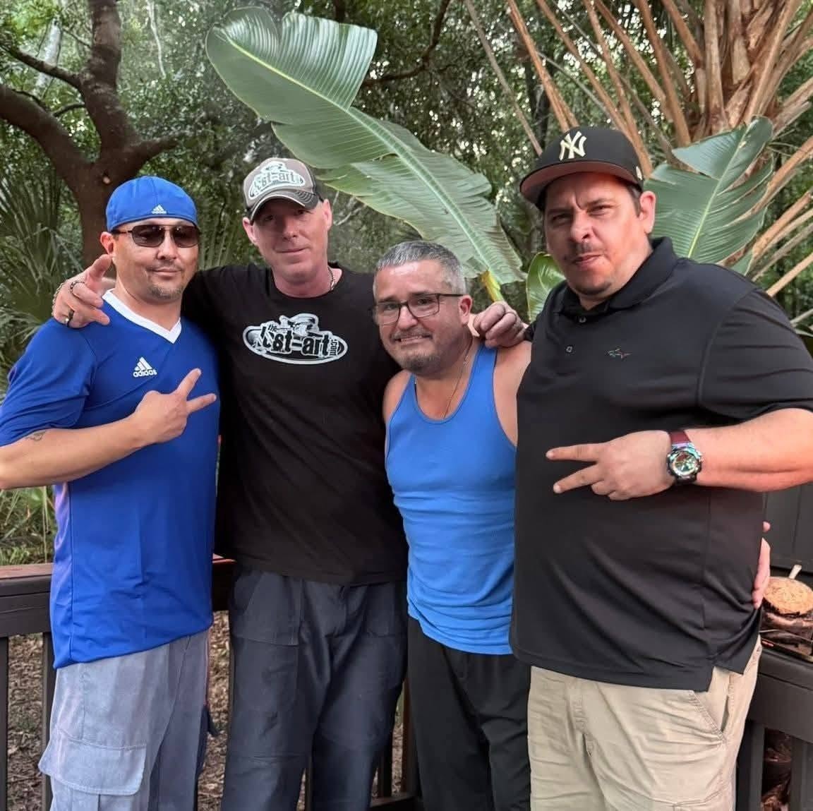 Four people including DJ Natural Nate® in The-Lost-Art.com black shirt outdoors surrounded by tropical plants in Homosassa Florida May 2026
