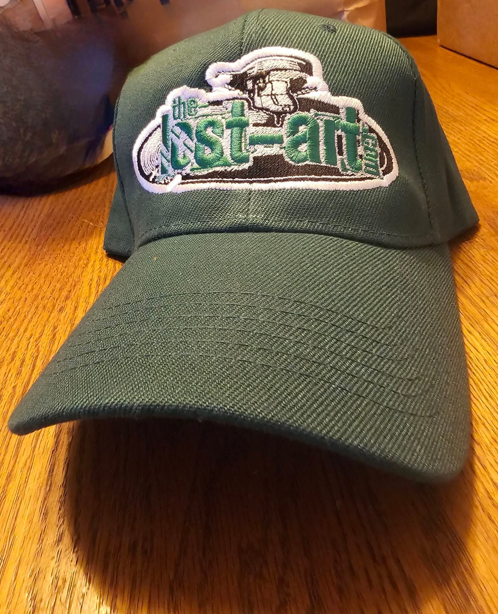 Green The-Lost-Art.com embroidered cap on a wooden table, DJ Natural Nate® Florida show May 2026