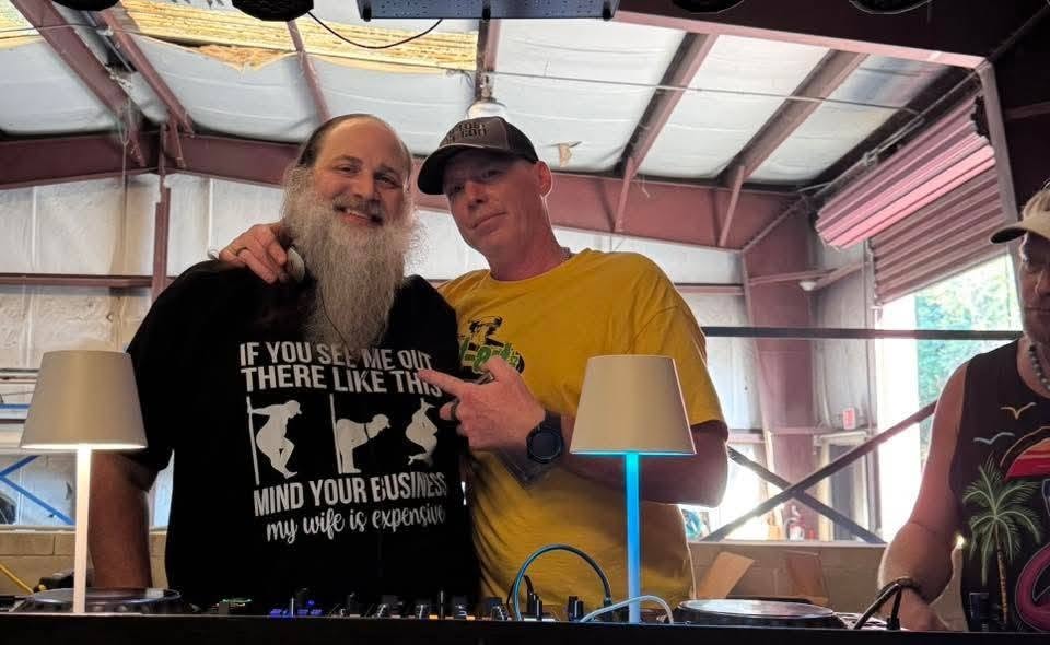DJ Natural Nate® in The-Lost-Art.com yellow shirt standing at the DJ decks with a friend at the Florida underground show May 2026