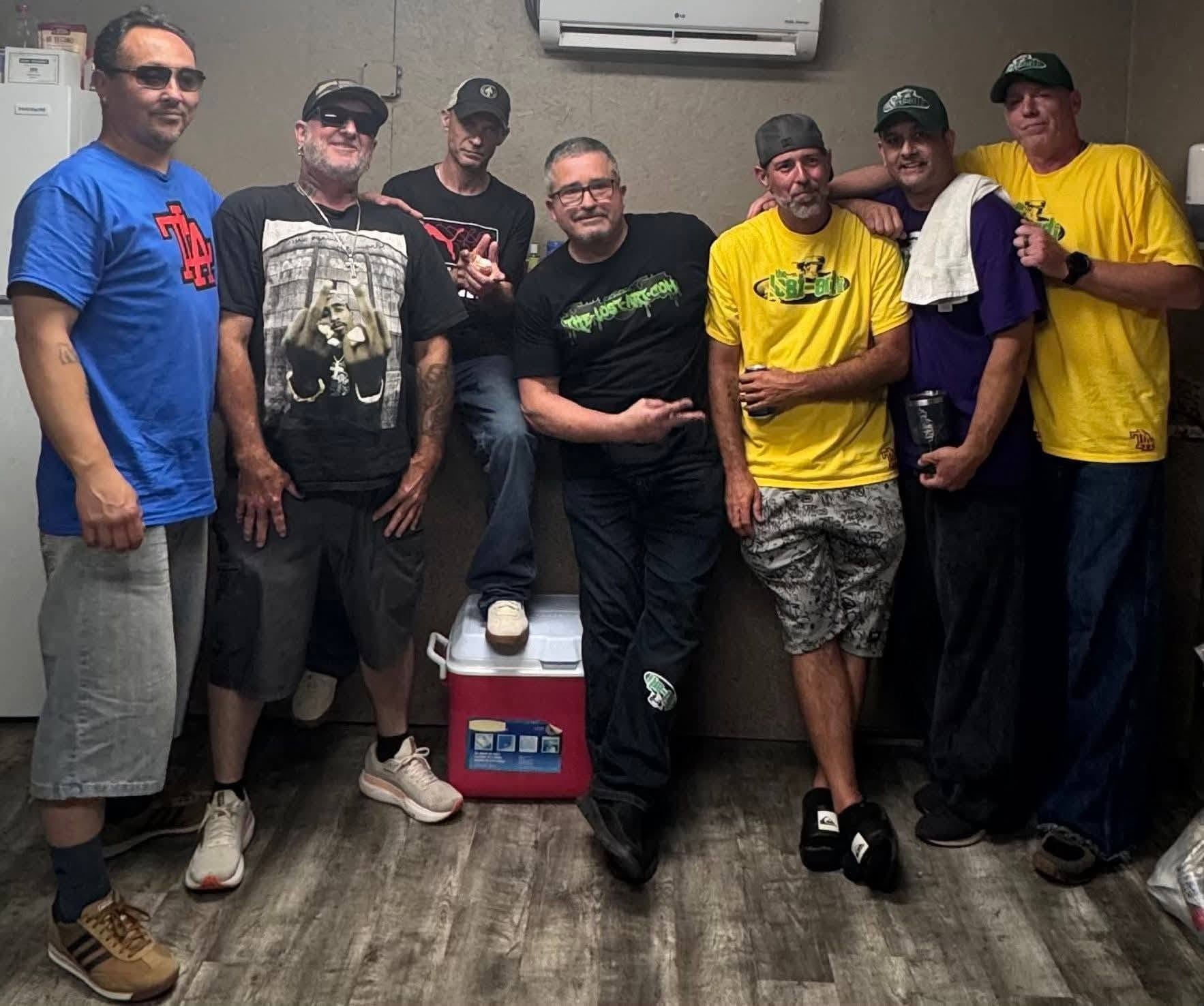 Seven people including DJ Natural Nate® in The-Lost-Art.com black shirt gathered indoors at the Florida underground show May 2026