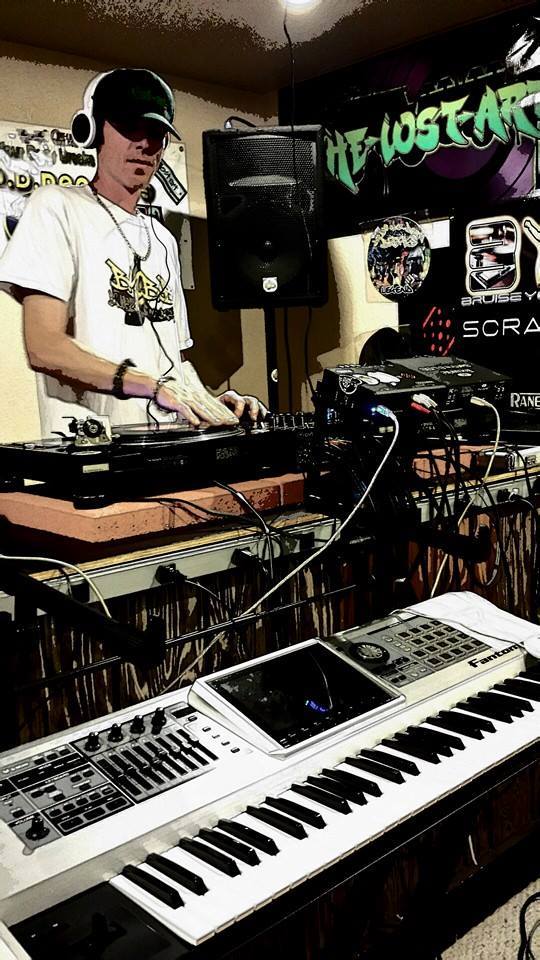DJ Natural Nate® on the turntables at The-Lost-Art.com studio, BYBB shirt, Roland Fantom in the foreground, The-Lost-Art.com graffiti banner behind him